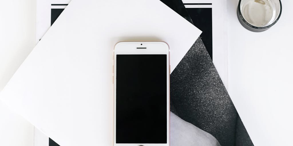 An artistic flat lay of a smartphone displaying the Slack app, surrounded by marketing materials like charts, graphs, and sticky notes. The background is a wooden desk with a plant and a coffee mug, creating a cozy yet professional vibe. This image symbolizes the integration of digital communication in marketing strategies.